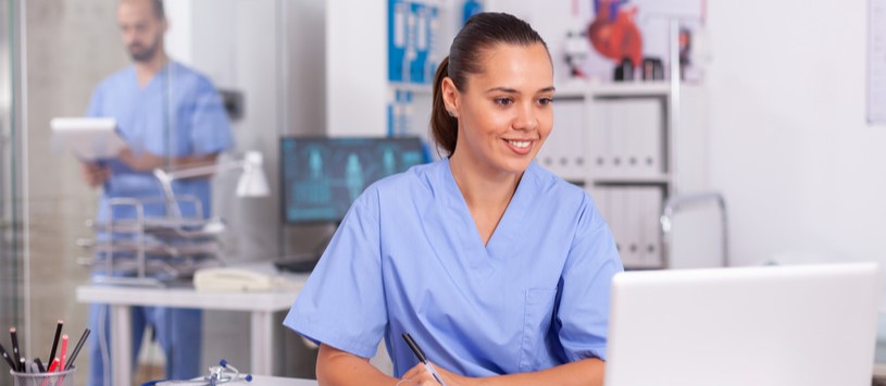 Health Information Administration professional working on a laptop in a medical office setting.